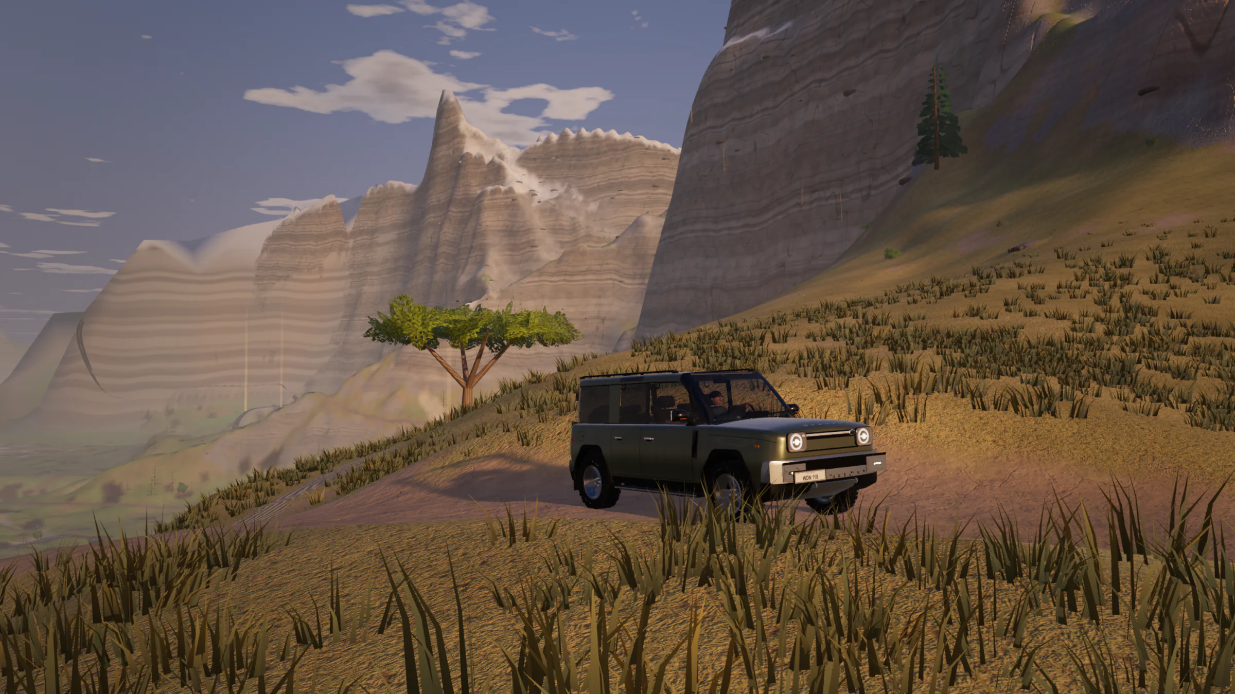 A green Warden 110 4x4 on a dirt trail across a grassy slope, striped canyon walls and a lone acacia behind it, in late-afternoon light